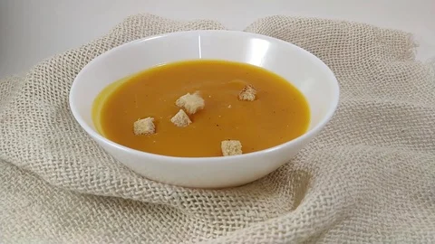 Pumpkin soup hard chuks falling into white plate Stock Footage 104547930