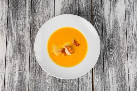 Pumpkin soup with shrimps in a plate on wooden background. Top view, close-up Stock Photos