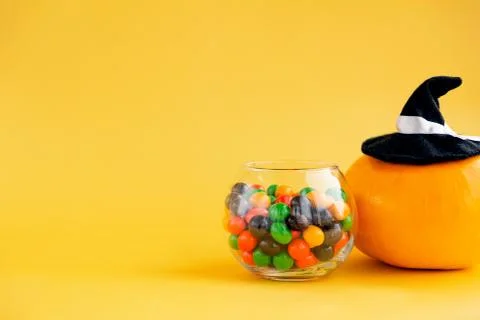 A pumpkin in a witch's cap and a round jar with multi-colored sweets on a yel Stock Photos