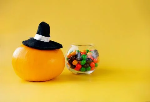 A pumpkin in a witch's cap and a round jar with multi-colored sweets on a yel Stock Photos
