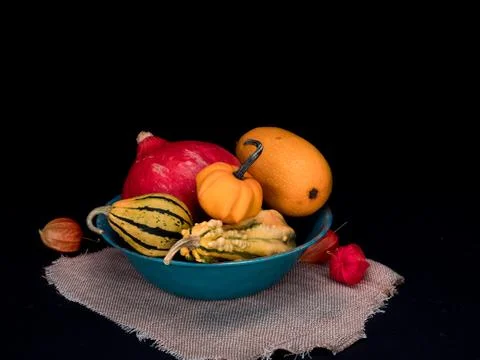 Pumpkins of different color and shape in a bowl black background Stock Photos
