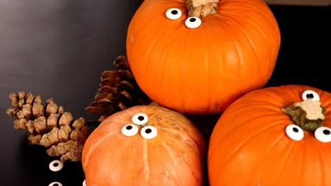 Pumpkins, googly eyes, pinecones create humorous Halloween scene. Vibrant autumn Stock Photos