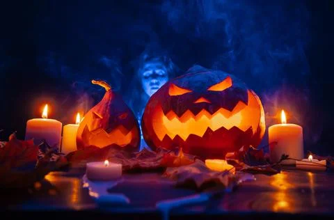 Pumpkins in smoke with carved faces by candlelight with a blue ghost. Stock Photos