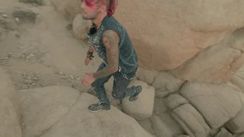 A Punk-style guy climbs up the rocks in a barren valley to reach a Goth girl 스톡 동영상 293275476