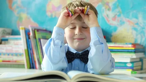 A pupil of a junior school twists his eyes in class. Funny schoolboy.  Stock Footage 77747739