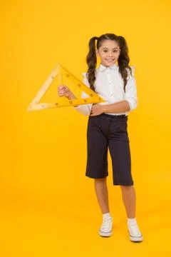 Pupil solving geometric problems. Cute small pupil holding triangle on yellow 스톡 사진