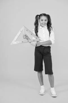 Pupil solving geometric problems. Cute small pupil holding triangle on yellow Stock Photos