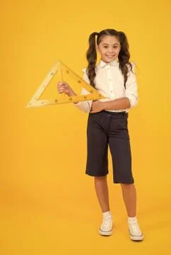 Pupil solving geometric problems. Cute small pupil holding triangle on yellow Stock Photos