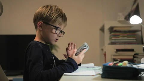Pupil at a write table picks up a phone, surf net and responds to a text Stock Footage 322516954
