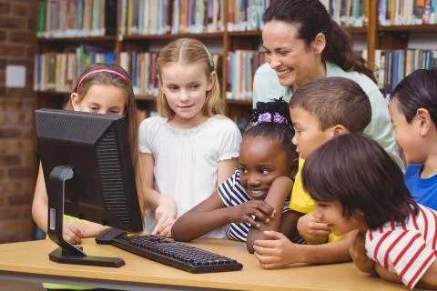 Pupils and teacher in the library using computer 스톡 사진