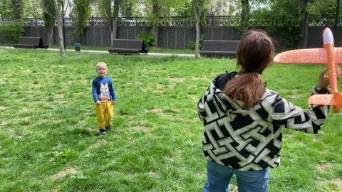 Pure Joy: Child Eagerly Awaits as Adult Prepares Toy Plane in Sunny Park Stock Footage 312313288