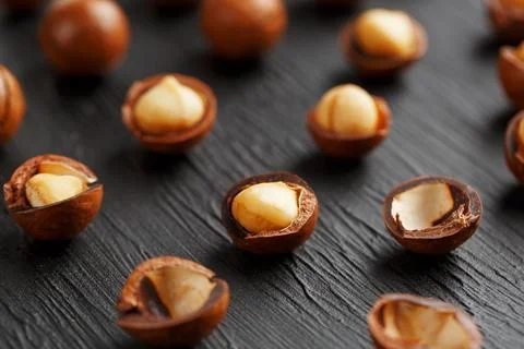 Purified and shell repeats macadamia nuts on black textural stone backgroun.. Фото