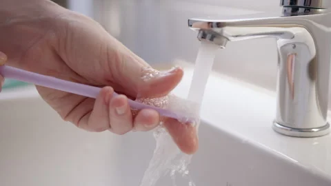 Purple brush is washed under running water in bathroom. Daily routine of Stock Footage 255881702