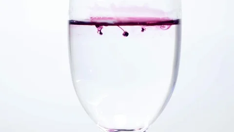 Purple ink dropping into glass of plain water Stock Footage