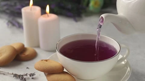 Purple tea from a white teapot is poured into a white mug Stock Footage