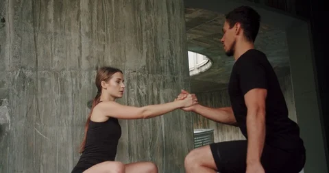 Purposeful sportive couple doing training exercises squatting connected hands Stock Footage 123662523
