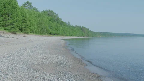 Push in above pebble beach of forested coastline of Lake Superior in summer Stock Footage 218399384