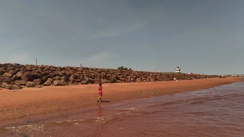 Push Back Drone Woman Walking on Red Sand Beach, PEI Stock Footage 341748890