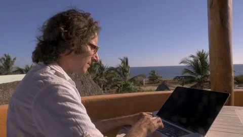 Push out of man using laptop computer at home office overlooking beach Video stock 80136360