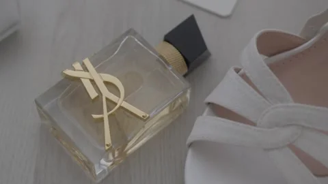 Push In Shot of YSL Libre Perfume Bottle with White Heels on Surface Stock Footage 334843248