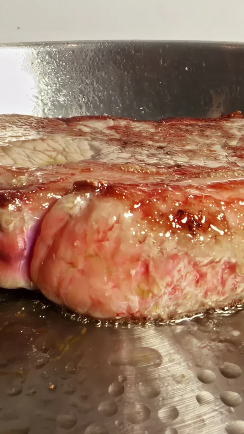 Push-in vertical social ratio close-up video of steak sizzling in a pan Stock Footage 336946139