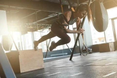 Pushing The Limits. Young athletic strong woman in sportswear doing TRX workout Stock Photos