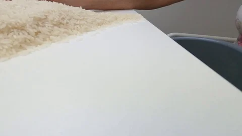 Pushing the raw white basmati rice grains from the white table into the pan. Stock Footage 128846412