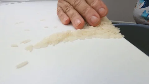 Pushing the raw white basmati rice grains from the white table into the pan. Stock Footage 128846481