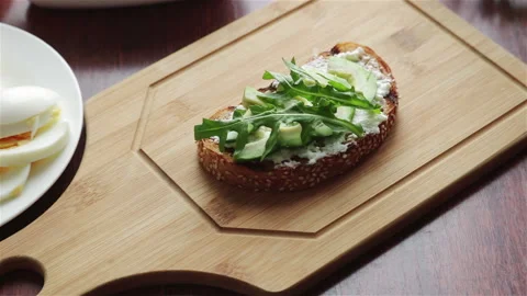 Put arugula leaves and cherry tomatoes halves on toast with cream cheese avocado Stock Footage 155893110