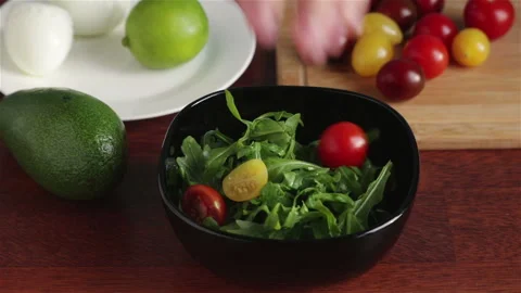 Put cherry tomatoes halves in to bowl with arugula salad leaves Vidéo 115083200