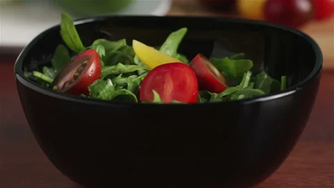 Put cherry tomatoes halves in to bowl with arugula salad leaves Stock Footage 155893129