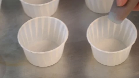 Put the dough into paper cups. Hand pouring cake dough into muffin tray Stock Footage 86764516