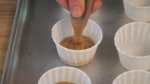 Put the dough into paper cups. Hand pouring cake dough into muffin tray Stock Footage 86765576