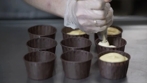 Put dough into paper cups. Hand pouring cake dough into muffin tray Stock Footage 96141330