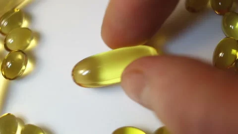 Put a large oval shiny transparent yellow capsule on a white table. Real-time, c Stock Footage 145108326