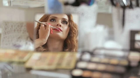Put makeup on. Beautiful young redhead woman putting her makeup on in front of Stock Footage 93688722