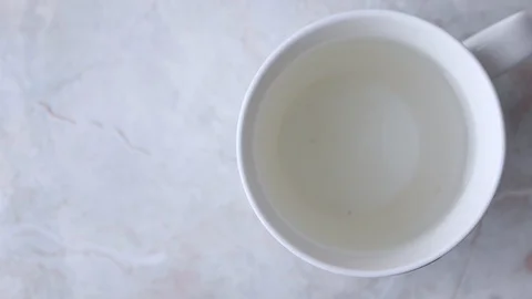 Put pyramid bag with fruity tea in white cup with hot water on marble backgro Stock Footage 119567647