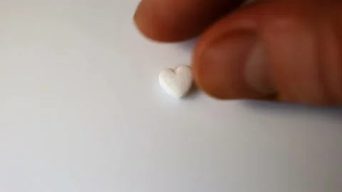 Put a small white pill in the shape of a heart on a white background. Close-up, Stock Footage 145374628