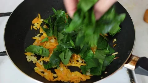 Put spinach in frying pan with onion and carrot cooking Stock Footage 237368186