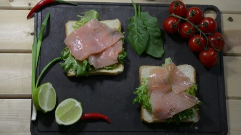 Puts pieces of fresh red fish on lettuce. Two toasts and spinach leaves. slide Stock Footage 122490537