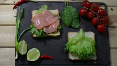 Puts slices of fresh red fish on lettuce. Two toasts and spinach 스톡 동영상 122490348