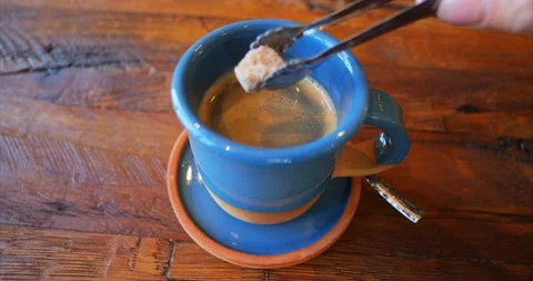 Puts the sugar into a blue cup with black coffee stands on a brown wooden table Stock Footage 229951865