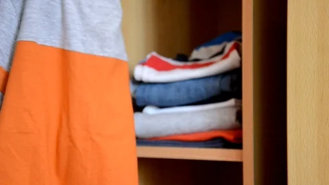 Puts things clothes in a closet on a shelf, multi-colored t-shirts, wardrobe Vidéo 125229922