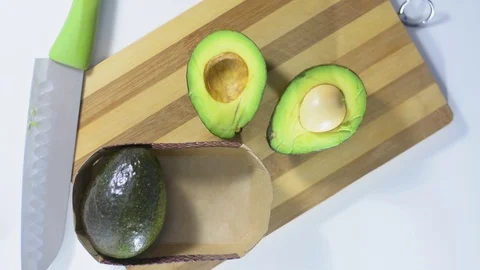 Puts two slices of fresh green avocado on a kitchen cutting board Stock Footage 122555978