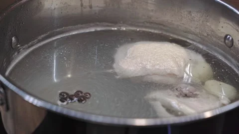 Putting allspice, bay leaf and turmeric in a chicken thigh broth in silver pot Stock Footage 329646578