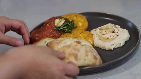 Putting bread on a plate with hummus and tomatoes, 4k, real time Stockbeeldmateriaal 248542260