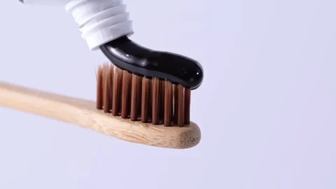Putting charcoal toothpaste on bamboo toothbrush on white background. Video stock 276155968