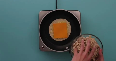 Putting chicken on a slice of cheese, shredded cheese, and a tortilla 1 Stock Footage 132203750