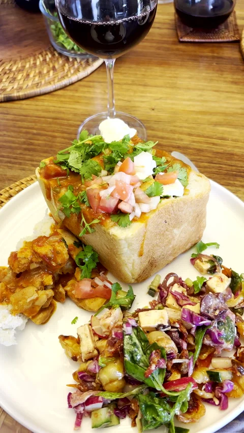 Putting chopped tomato and onion salsa garnish onto bunny chow (chicken curry) Stock Footage 342576399