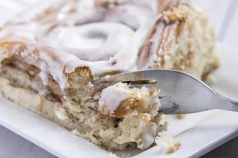 Putting a fork into a cinnamon roll. Stock Photos